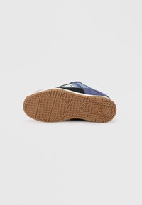 Shoe sole in brown rubber with a textured grip pattern. Upper features blue fabric and black accents with logo detail near the heel.