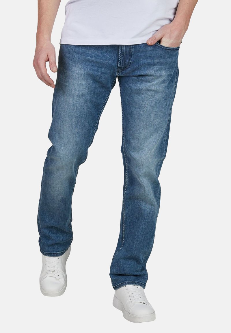 Jeans de mezclilla azul oscuro con corte recto, que presentan un diseño clásico de cinco bolsillos y un ligero desgaste. Combinados con zapatillas blancas.