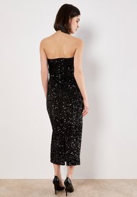 Schwarzes, paillettenbesetztes, trägerloses Kleid mit figurbetontem Schnitt, knielang und mit seitlichem Schlitz, das eine glatte, glänzende Textur und ein rückenfreies Design aufweist.