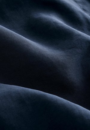 Tessuto blu navy con una texture liscia, che mostra dolci onde e pieghe, indicando un materiale leggero e flessibile.