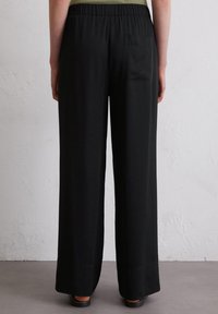 Zwarte broek met wijde pijpen, een elastische tailleband en een enkele achterzak, gemaakt van een gladde stof, ideaal voor casual kleding.