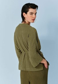 Oliven grønt tekstureret cardigan med bælte i taljen, trekvartærmer og løs pasform, parret med matchende teksturerede bukser.