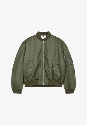 Alyvuogių žalumo bombonešio stiliaus striukė su priekiu užtrauktuku, dviem kišenėmis su spaudėmis, ribotu rankogaliu, apykakle, apačia ir užtrauktuku kairiajame rankove.