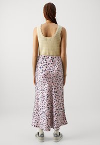 Heklet, ermeløs topp i beige, kombinert med et langt, flytende rosa skjørt med blomstermønster i svart, hvitt og blått.