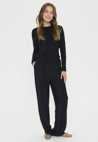 Námornícky modrý top s dlhým rukávom a priliehavým pásom, spárovaný s voľnými, zodpovedajúcimi nohavicami vyrobenými z mäkkého materiálu. Doplnkovými sú ležérne slip-on topánky so cvočkami.