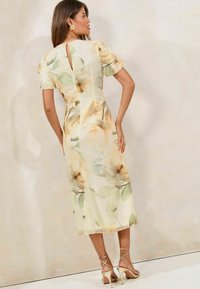 Blumenkleid mit kurzen Ärmeln, Schlüsselrücken-Detail, cremefarbenem Hintergrund, großen beigen Blumen und grünen Blättern. Kombiniert mit beigen Riemchen-Heels.