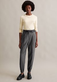 Blusa de manga longa amarelo-claro combinada com calças cinzas de risca de giz de cintura alta, com punho elástico e cinto. Mocassins pretos completam o visual.