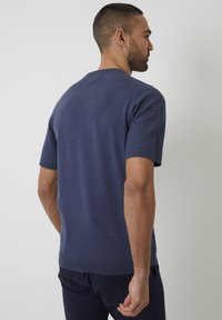 Kurzärmliger, navyblauer Strickpullover mit strukturiertem Muster an den Schultern und gerippten Säumen. Leicht taillierte Passform, glatte Stoffstruktur.