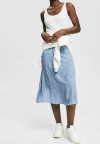 Falda midi azul con estampado floral y textura suave, combinada con una camiseta sin mangas blanca y un suéter ligero atado a la cintura, completada con zapatillas blancas.
