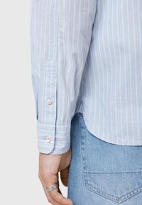 Lyseblå stribet skjorte med knaplukning vedærmerne, featuring lodrette striber og en glat tekstur, parret med lyse denim.
