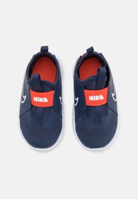 Marinblå Nike slip-in skor med röda detaljer, en texturerad tygöverdel och vita sulor; har ett framträdande logotagsrem över fotryggen.