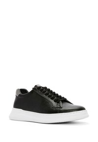 Baskets en cuir noir avec un bout arrondi, lacets noirs et une semelle blanche contrastante. Présente une texture lisse et un design élégant.