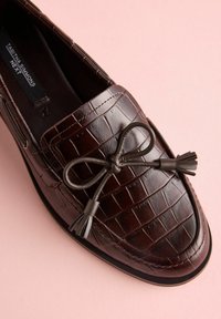 Mocasini maro din piele cu textură în relief de tip croc, având un detaliu decorativ cu fundă și ciucuri pe partea superioară. Talpă de cauciuc.