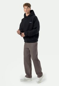 Melns kapucnis ar teksturētu audumu, ribveida aprocēm un mazu logotipu uz krūtīm. Savienots ar pelēkām biksēm un baltām kedām.