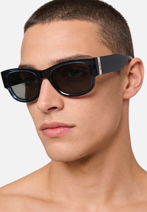 Occhiali da sole rettangolari neri con lenti scure, caratterizzati da una montatura spessa e aste accentuate. Design minimalista con marchio metallico sul lato.
