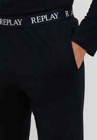 Schwarze Baumwoll-Jogginghosen mit einer weichen Textur, ausgestattet mit einem weißen "REPLAY"-Logo am Bund und Seitentaschen für zusätzlichen Nutzen.