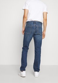 Blå denimjeans med rakt snitt, femficksdesign och synliga sömmar. Kombinerade med en enkel vit t-shirt och vita sneakers.