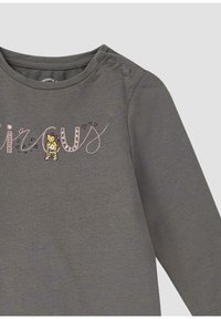Grijze shirt met lange mouwen met de tekst "circus" in speelse roze en zwarte borduursel, met een cartoonleeuw-illustratie naast de tekst. Drukknoopjes op de schouder.