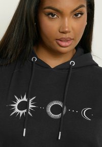 Felpa nera con grafiche celestiali bianche: sole, luna piena e luna crescente, con lacci e hardware in tonalità argento. Tessuto morbido.