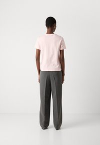 Helles pinkes Baumwoll-T-Shirt mit kurzen Ärmeln und rundem Ausschnitt, kombiniert mit grauen, maßgeschneiderten, weiten Hosen.