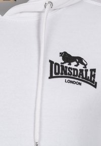 Fehér kapucnis pulóver, húzókával, fekete oroszlán logóval és "LONSDALE LONDON" felirattal. Az anyaga lágy és struktúrált.