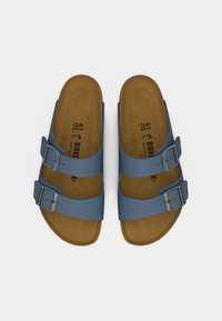 Ζευγάρι σανδαλιών με καφέ σόλες, μπλε δερμάτινα λουριά και μεταλλικές αγκράφες, φωτογραφημένα από ψηλά σε λευκό φόντο.