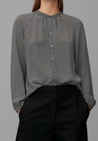 Svart- och vitt mönstrad blus med rund halsringning, knäppning fram och långa ärmar, tillsammans med svarta byxor.