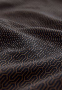 Textielstof met een abstract geometrisch patroon in goud op een donkerblauwe achtergrond, met een gladde, licht gestructureerde oppervlakte.