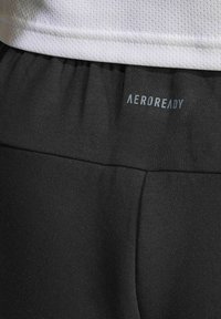 Svarte træningsbukser lavet af strækbart materiale med en glat tekstur. Har en bred talje med "AEROREADY" logo i lyseblå.