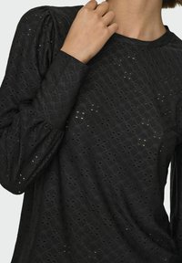 Blusa nera con motivo ricamato testurizzato e dettagli a taglio. Le maniche sono leggermente gonfiate per aggiungere dimensione.