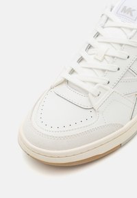 Baskets en cuir blanc avec accents en suède, détails perforés et lacets plats. Dotées d'une semelle en caoutchouc de couleur claire et d'un design distinct du panneau latéral.