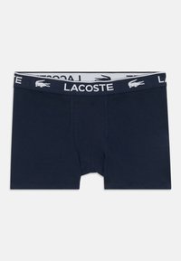 Pantaloni boxer blu navy con una cintura testurizzata bianca che presenta "LACOSTE" e un piccolo logo coccodrillo. Realizzati in un morbido tessuto elasticizzato.