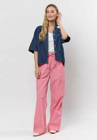 Denim košeľa na gombíky s krátkymi, prehodenými rukávmi cez biely tielko, skombinovaná s širokými nohavicami v ružových pruhoch a svetlými topánkami.