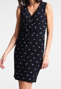 Czarna sukienka bez rękawów o fasonie kopertowym z niebieskim wzorem jaskółek. Posiada zwężoną w talii sylwetkę oraz gładką teksturę materiału.