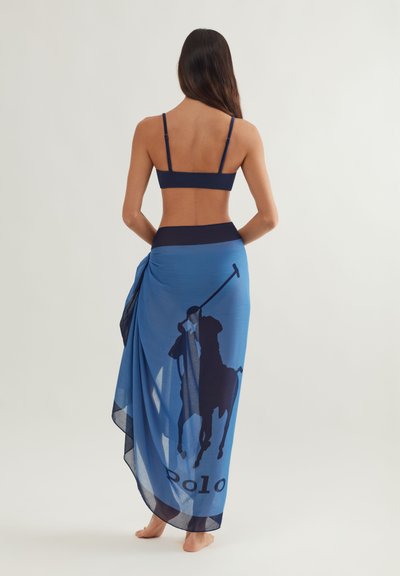 Μπλε διάφανο σαρόνγκ με γραφικό κέντημα ενός παίκτη πόλο σε σκούρο μπλε και το κείμενο "Polo" κατά μήκος του τελειώματος. Το ύφασμα έχει ελαφριά, ρέουσα υφή.