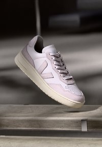 Ljusrosa sneaker med en slät läderövre, perforerad tå, vadderad krage och en vit gummisula. Har en enkel logotypdetalj.
