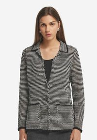 Svart och vit mönstrad cardigan med krage, fyra framknappar och två fickor. Strukturerat stickat tyg; långa ärmar.