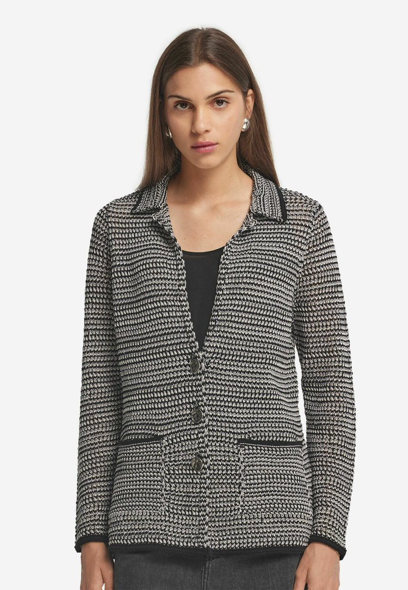 Svart och vit mönstrad cardigan med krage, fyra framknappar och två fickor. Strukturerat stickat tyg; långa ärmar.