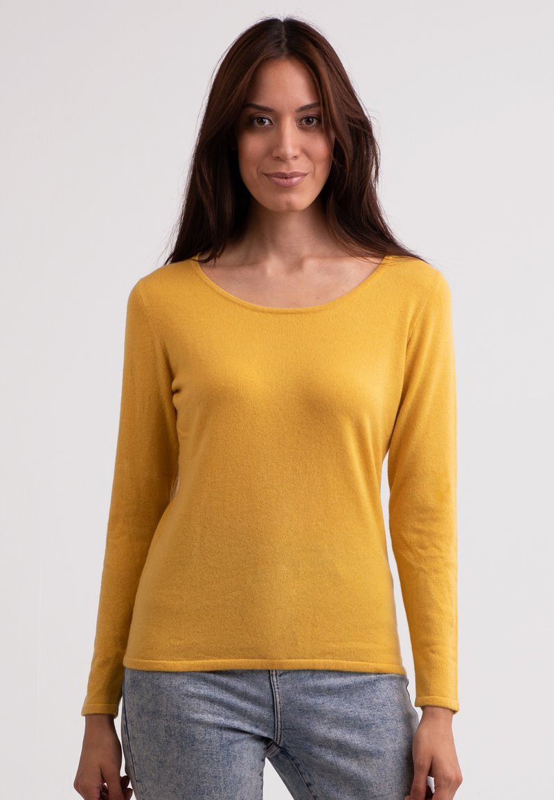 Langärmliger gelber Pullover aus weichem Strickstoff. Er verfügt über einen Rundhalsausschnitt und eine figurbetonte Silhouette. Getragen mit blauen Jeans.