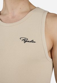 Beige tanktop med ribbestruktur og rund hals. Har en liten svart "Pegador"-logo på venstre side.
