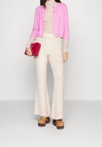 Vaaleanpunainen villa-neule, beige rypistyneenä päällikö, tekstuurilliset vaalean kermaiset leveälahkeiset housut ja tikkikuvioitunut punainen laukkukotelo. Ruskeat paksulautaiset kengät viimeistelevät asun.