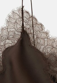 Primer plano de tela de satén marrón con delicado borde de encaje floral y finas tirantas sobre un fondo claro.