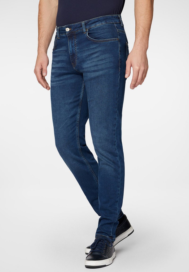 Jeans dżinsowe w ciemnoniebieskim kolorze o dopasowanym kroju, z zamkiem błyskawicznym i zapięciem na guzik. Dodatki obejmują kieszenie z przodu oraz subtelne efekty przetarcia.