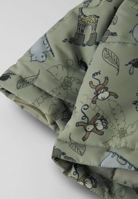 Un tissu vert doux avec des imprimés d'animaux de dessin animé, incluant des singes et des girafes, avec une texture lisse et des coutures piquées.