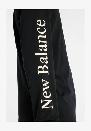 Sort langærmet t-shirt lavet af bomuld, med "New Balance" logo i stort hvidt skrifttype langs ærmet. Glat tekstur og standard pasform.