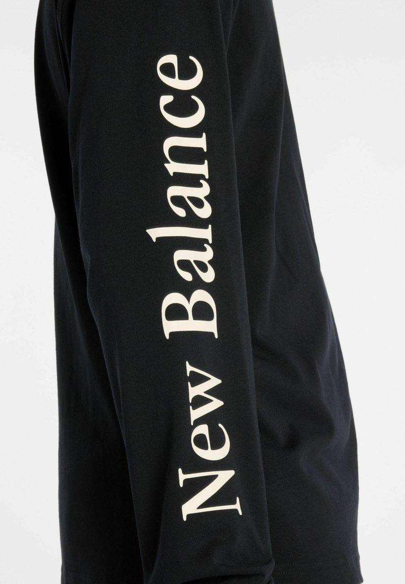 Zwarte lange mouwen T-shirt van katoen, met het "New Balance" logo in grote witte letters langs de arm. Soepele textuur en standaard pasvorm.