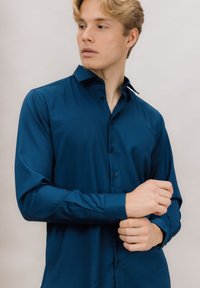 Mørkeblå langermet skjorte med knappet krage, glatt tekstur og skreddersydd passform, med en knappestolpe foran.