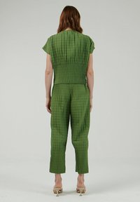 Groene gewatteerde jumpsuit met een aansluitend bovenstuk en wijdvallende broekspijpen, voorzien van korte mouwen en een geribbelde textuur. De achterkant toont elastische details.