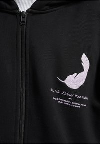 Zwarte hoodie met ritssluiting, met een wit geborduurde veer en de tekst: "Vive la Liberté. Vrijheid is de vrijheid om te leven zoals je wilt."