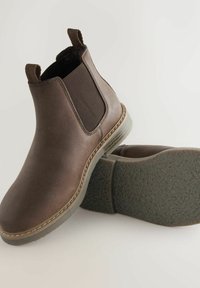 Bruna läderankelboots med elastiska sidopaneler, rund tå, platt gummisula och draganordningar för enkel påtagning. Texturerad yttersula.
